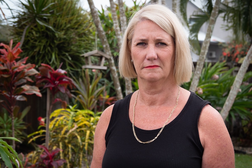 A woman stands on a palm tree beach and looks directly at the camera