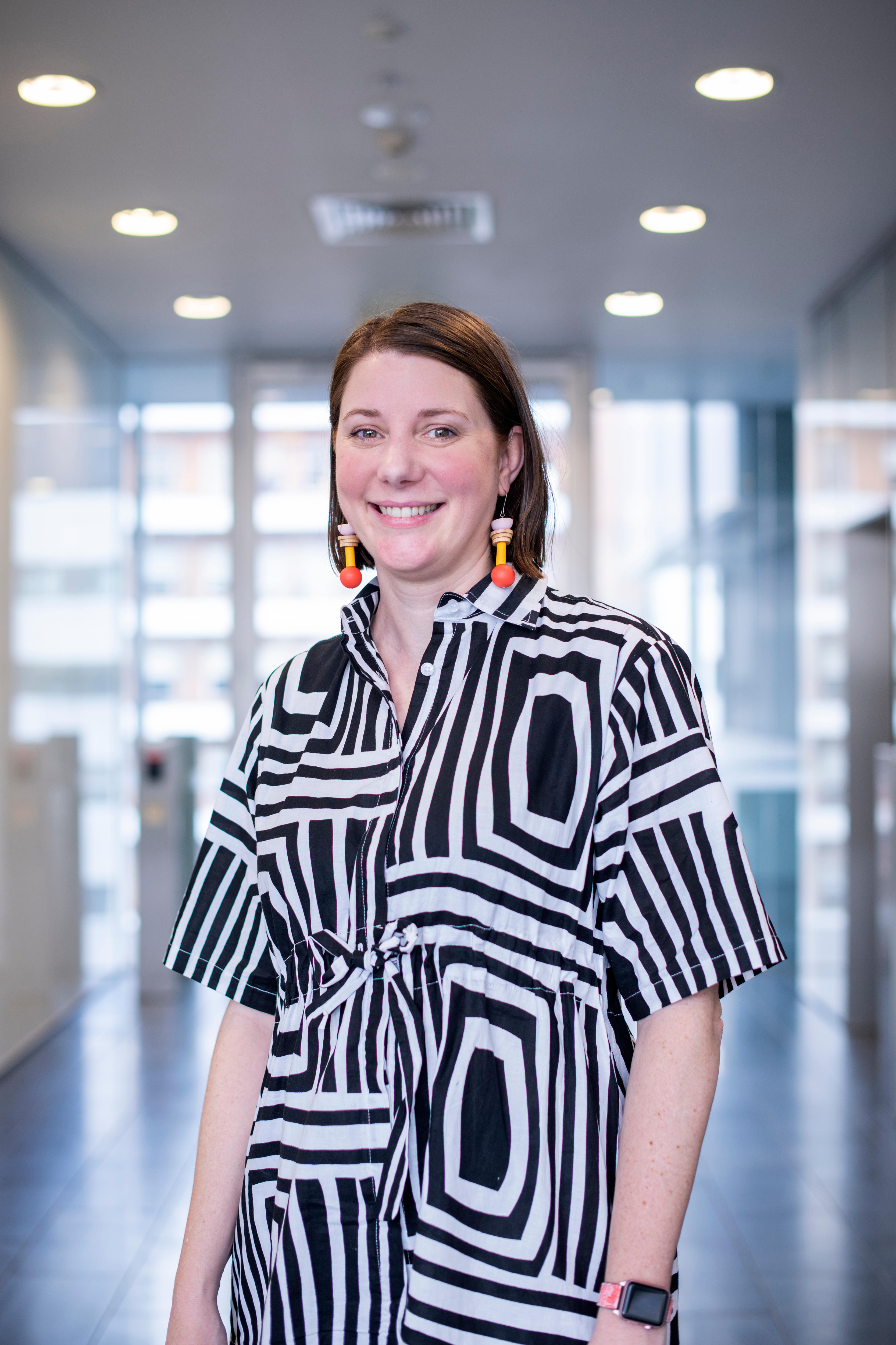 Woman wearing black and white patterned dress smiles while standing inside research lab.