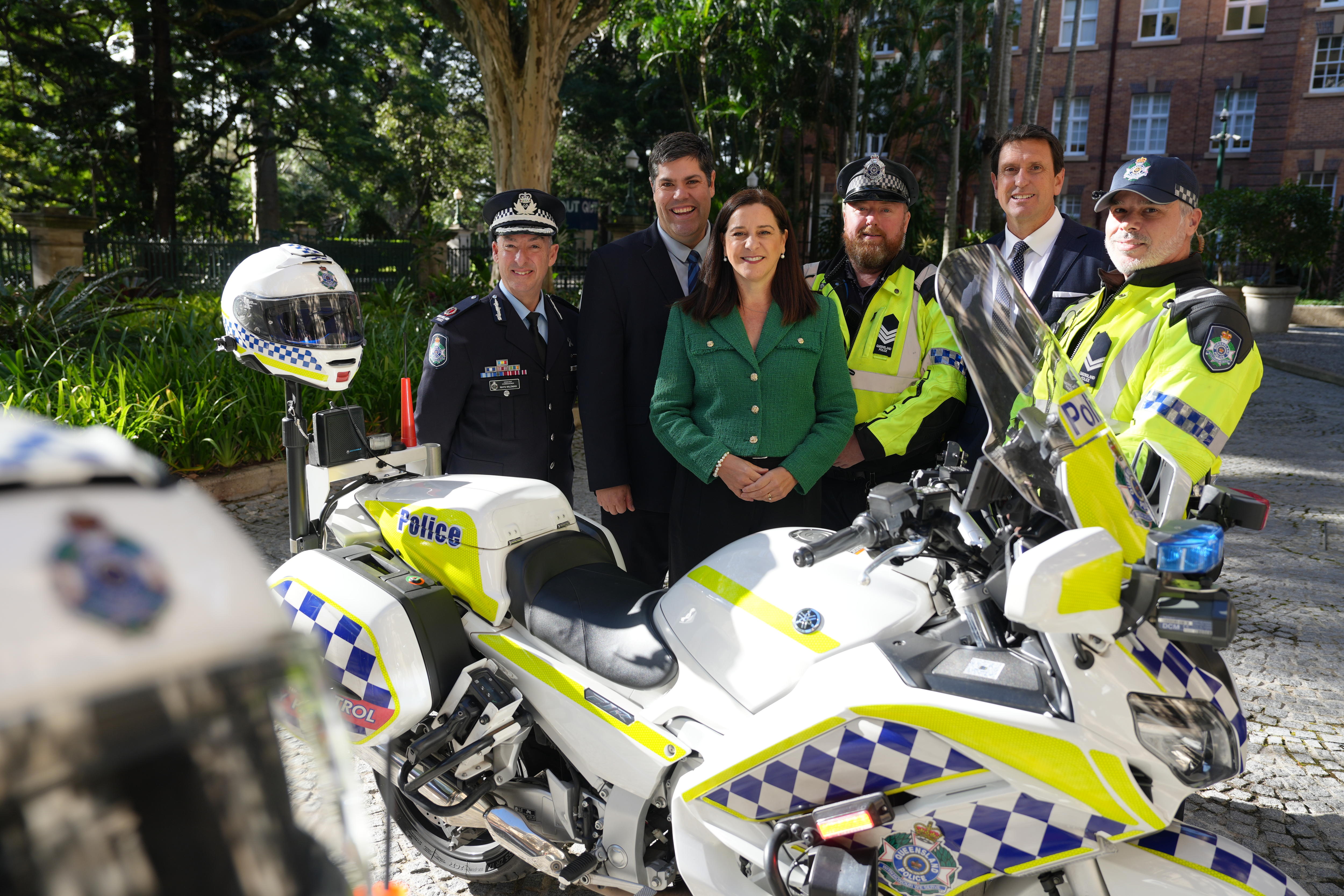 A woman and five men gathered in a group behind a police motorcycle.
