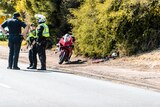 Police stand by a red motorcycle, jacket and helmet on the side of the road. 