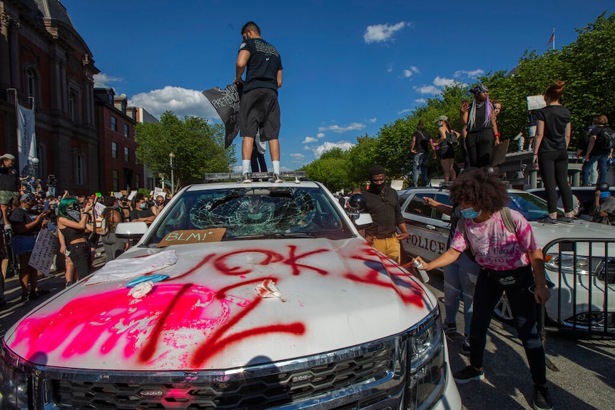 A man stands on a secret service vehicle which has been heavily vandalised.