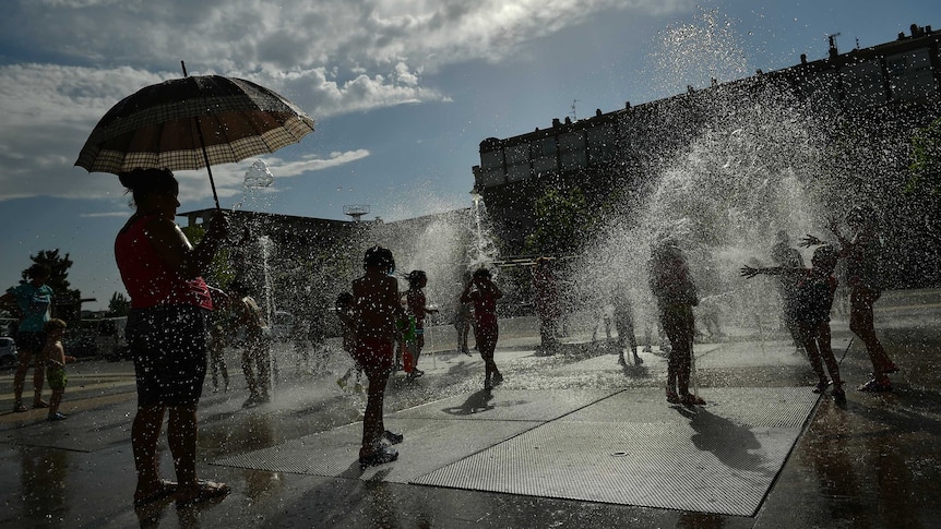 People cool off in a fountain as the sun shine behind them.