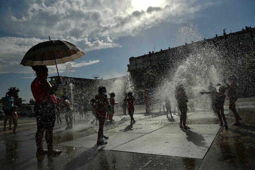 People cool off in a fountain as the sun shine behind them.