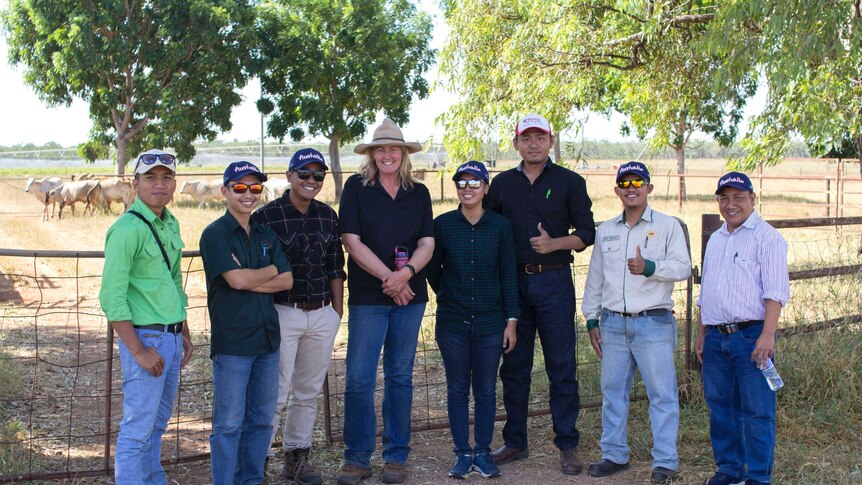 a group of men and women standing in a paddock with cattle behind.