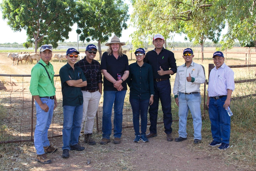 a group of men and women standing in a paddock with cattle behind.