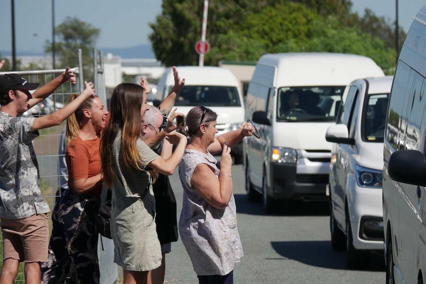 People wave as minibuses drive away