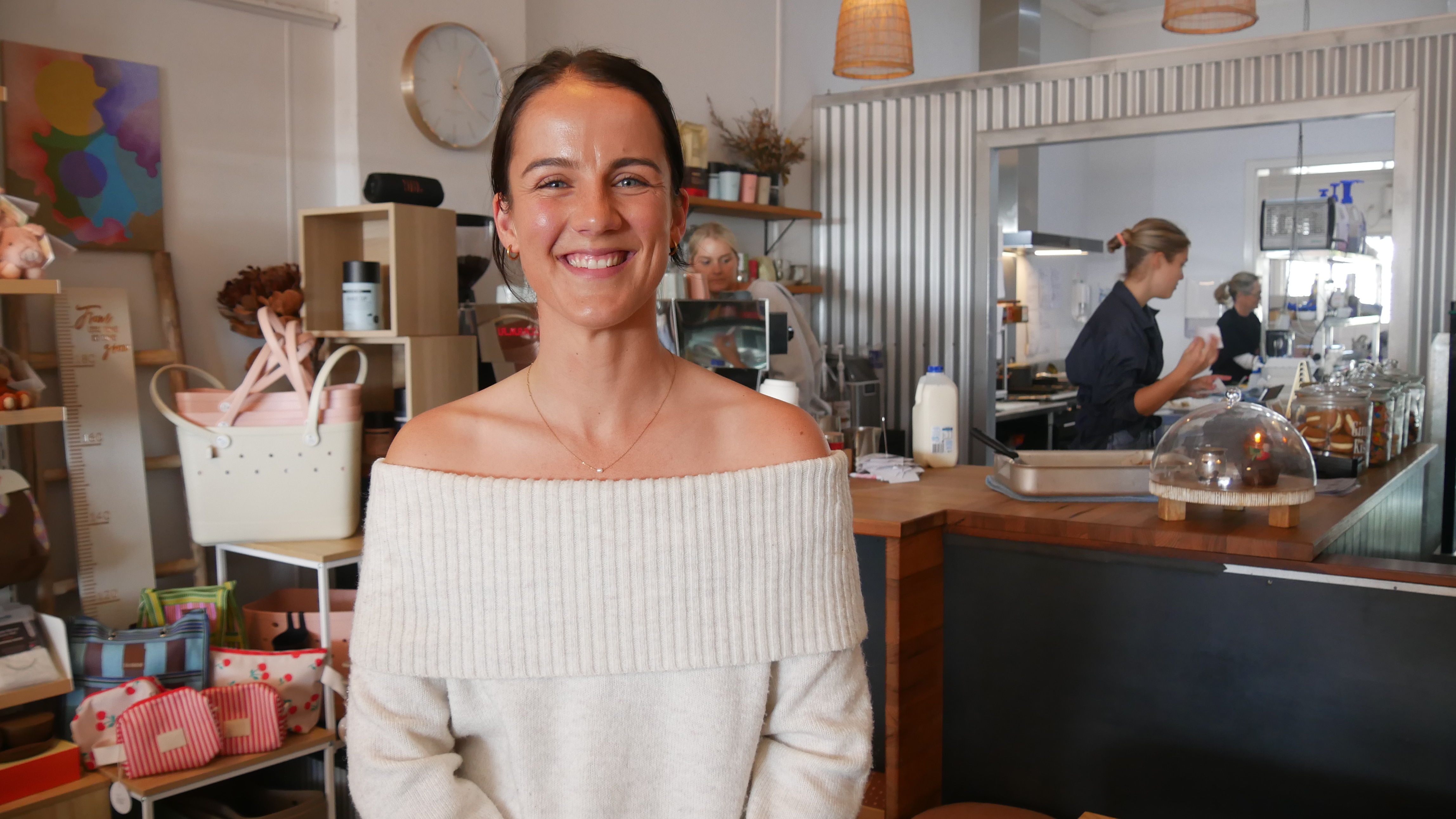 A girl in a cream jumper stands in front of a cafe counter.