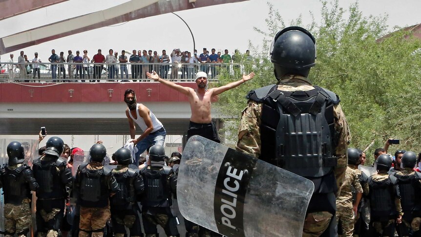 A man stands shirtless amid protesters facing riot police