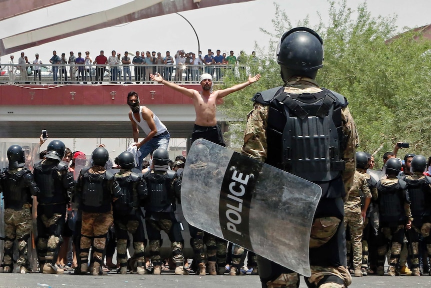 A man stands shirtless amid protesters facing riot police