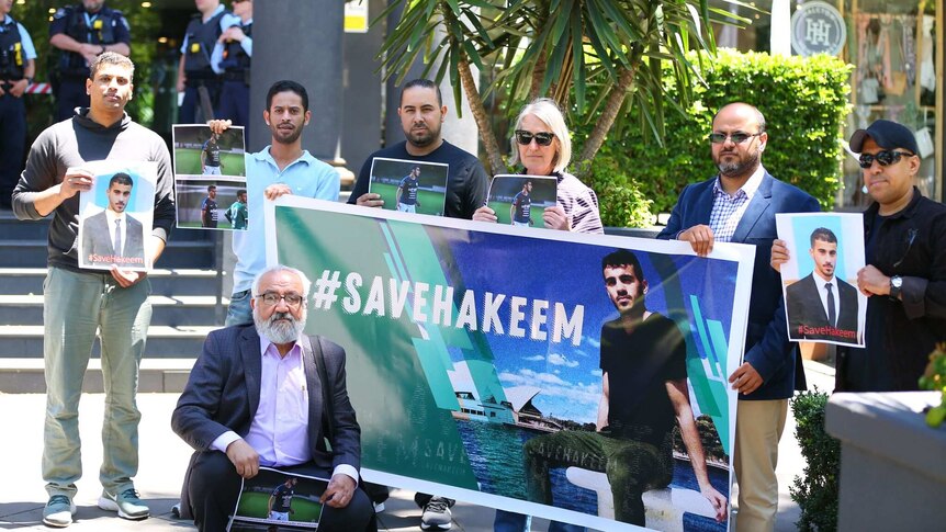 A group of seven campaigners holding #saveHakeem posters look to the camera during protest.