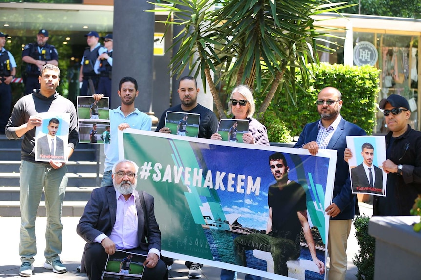 A group of seven campaigners holding #saveHakeem posters look to the camera during protest.