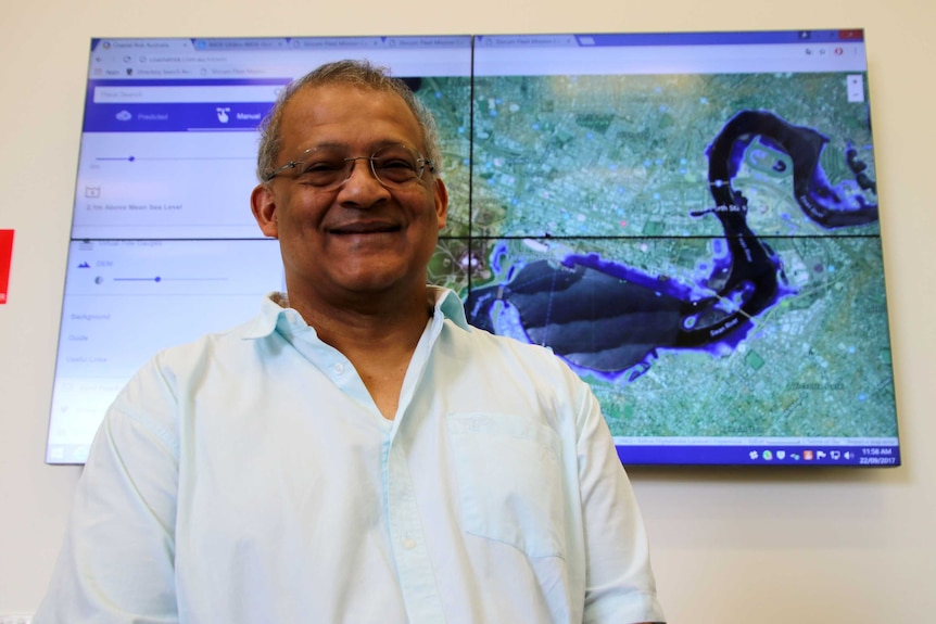 Man standing in front of a big screen with aerial view of Swan River.