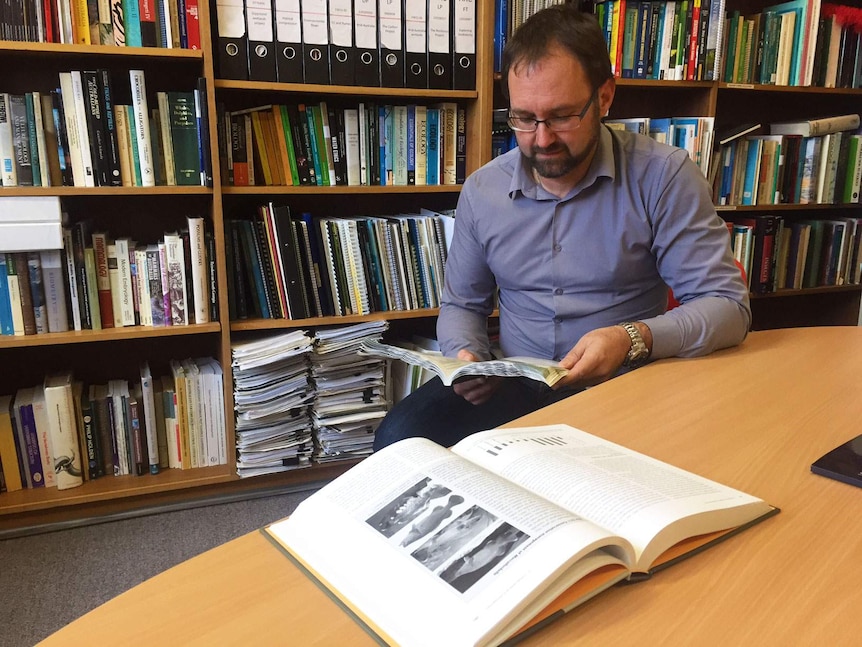 A man reads a book in a research library with a book about fish open in front of him.