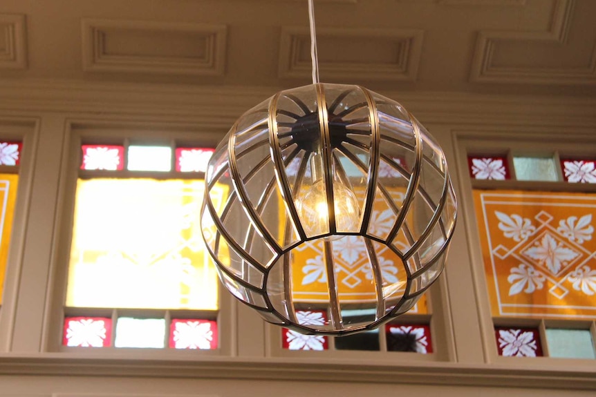 An intricate art deco light fixture hangs from the ceiling in front of stained glass windows