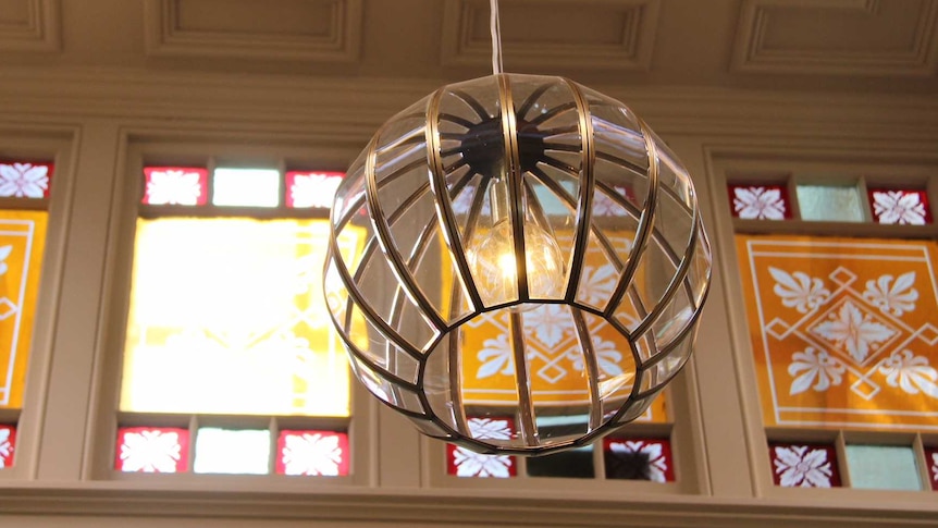 An intricate art deco light fixture hangs from the ceiling in front of stained glass windows