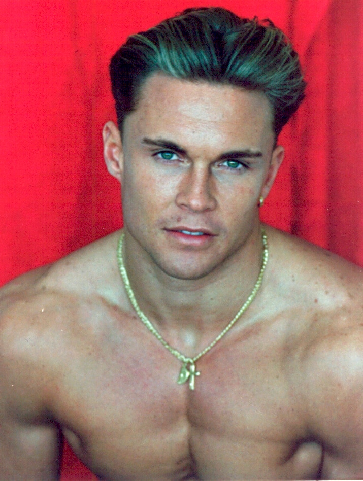 Brett Boyd without a shirt and wearing a gold chain poses for the camera in a modelling glamour shot.