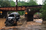 Car mangled by floodwaters sits under a bridge