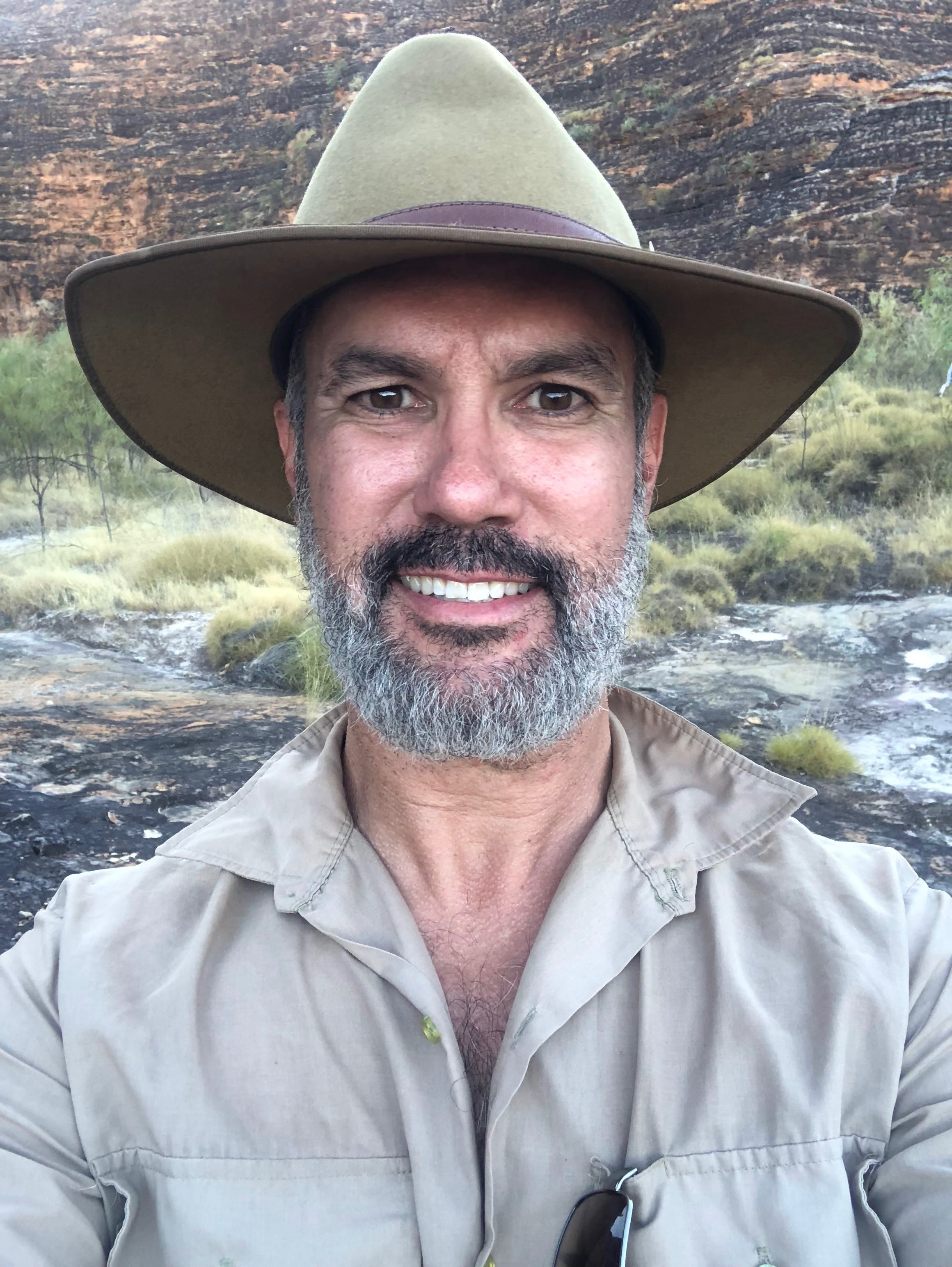 Un hombre con una barba gris y negra con un sombrero grande sonríe a la cámara