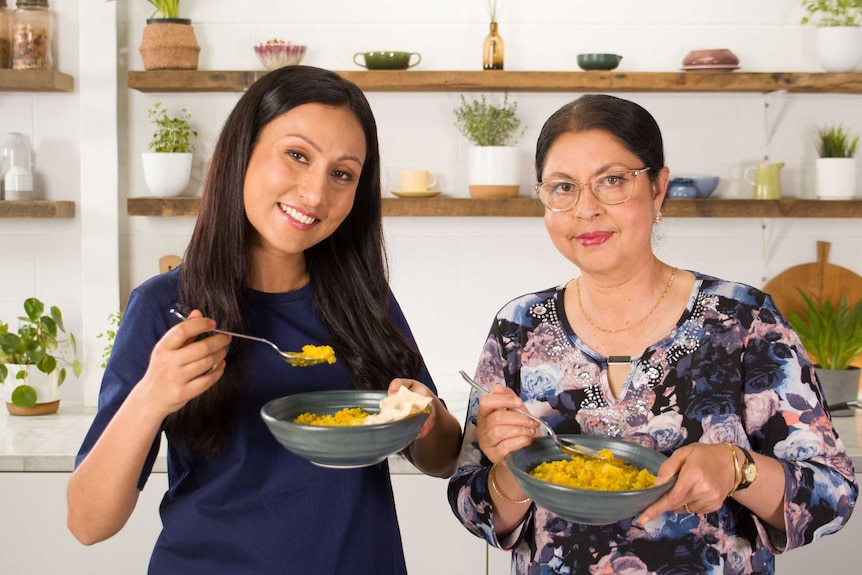 Urvi Majumdar and Sruti Majumdar present a yellow bowl of food in a kitchen.