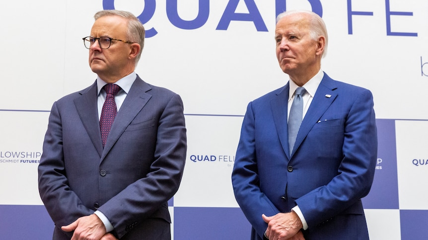 Anthony Albanese and Joe Biden stand beside each other in front of the Quad event signage. 
