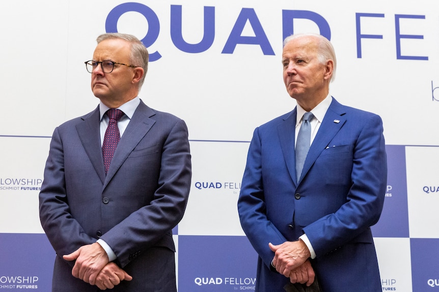 Anthony Albanese and Joe Biden stand beside each other in front of the Quad event signage. 