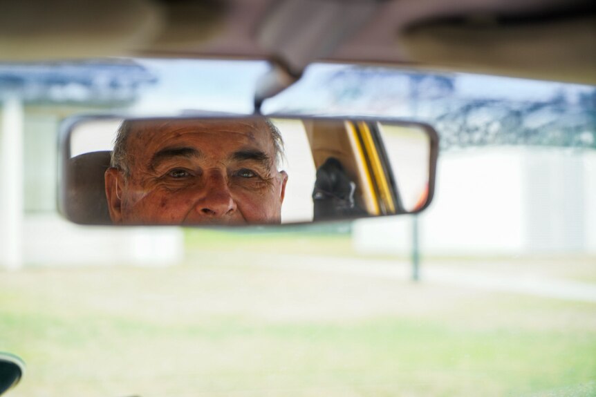 Man looking in rear-view mirror of car.