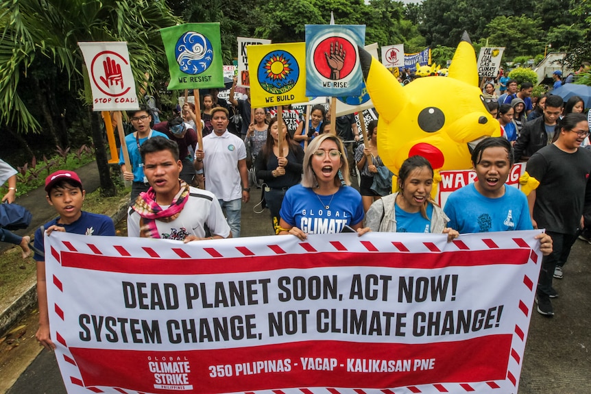 a group of protesters hold up a sign that says 'dead planet soon, act now! system change, not climate change'