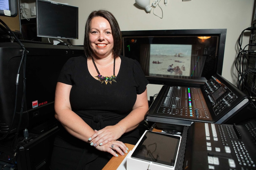 A woman in a control rooms smiles at the camera.