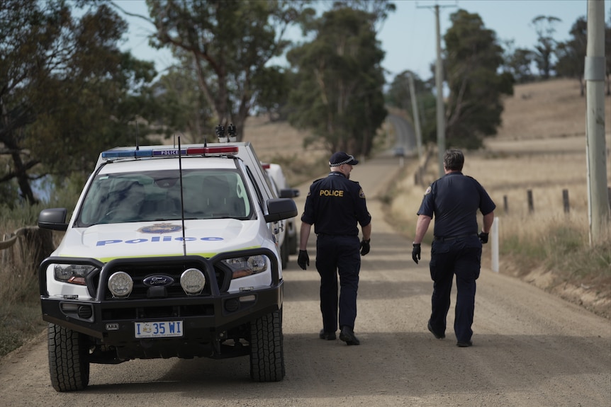 Tasmania Police walking up a dirt road with cars parked nearby.