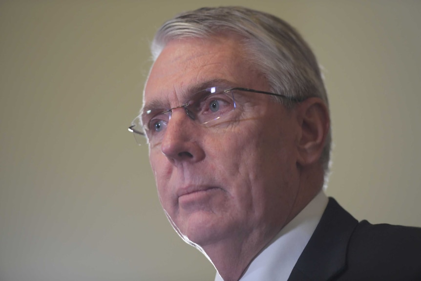 A man with glasses and grey hair speaks at a lectern