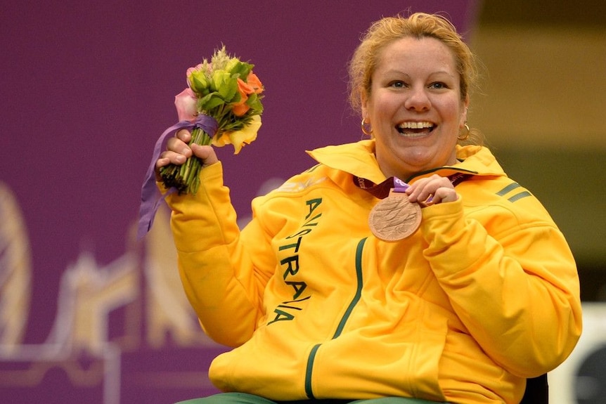Natalie Smith levanta su medalla y sonríe.