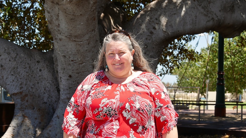 A woman in a red shirt smiling under a large tree. 
