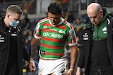 A South Sydney NRL player walks off the field injured in between two Rabbitohs staff members.