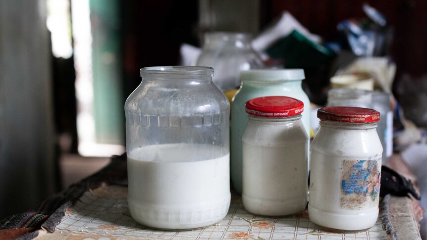 Jars of milk sit on a table inside a house.