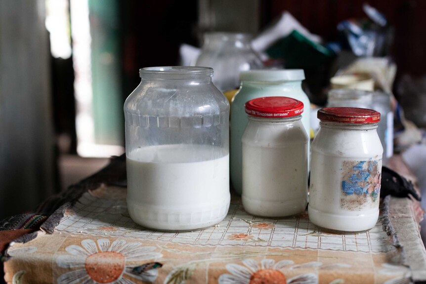 Jars of milk sit on a table inside a house.