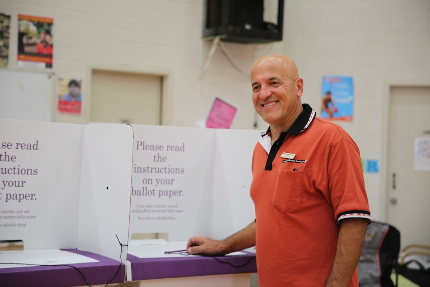Man stands next to polling booth smiling