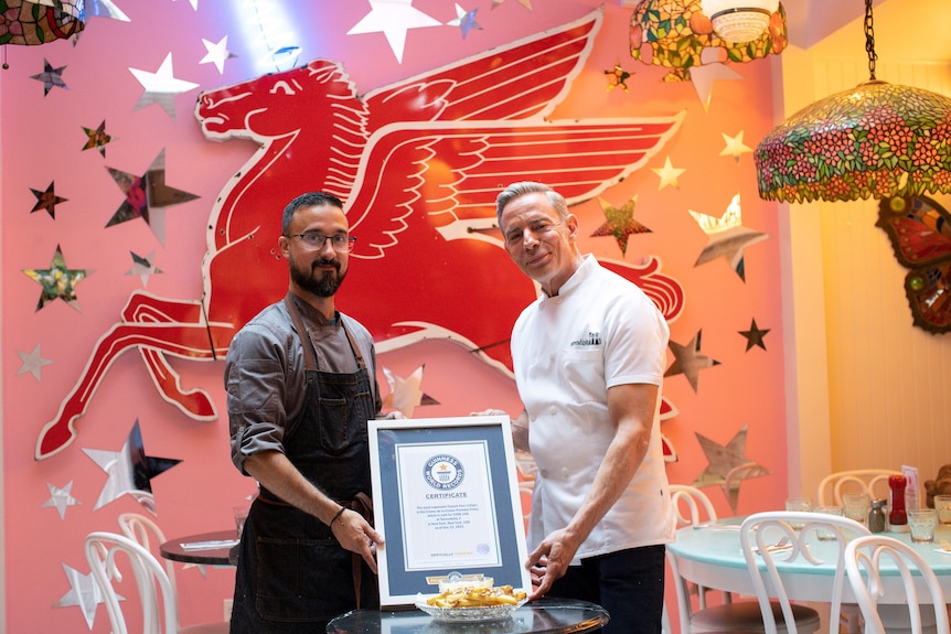 Two men pose for a photo in a pink restaurant, where they're holding their world record certificate. 
