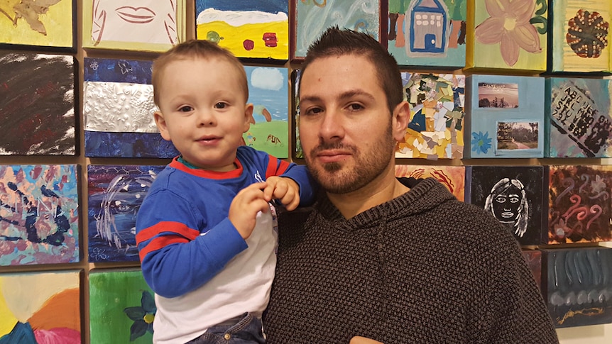 Man holding toddler in front of a wall of children's drawings