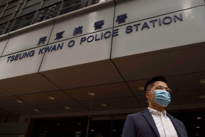 A man in a suit and medical mask stands outside a Hong Kong police building