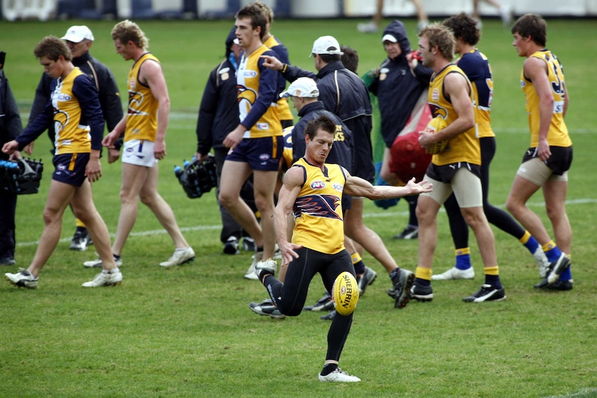 Ben Cousins kicks a football during West Coast Eagles raining with teammates walking behind him.