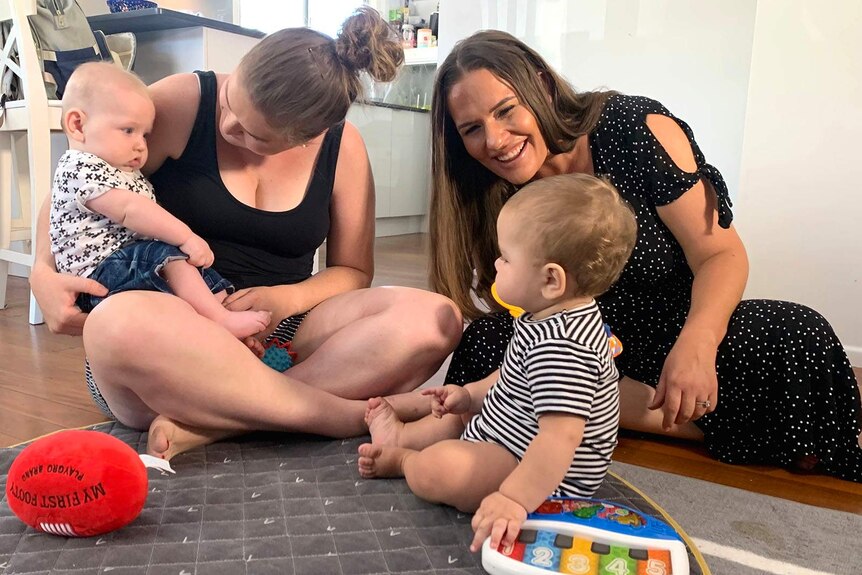 Two mothers playing on the floor with their babies
