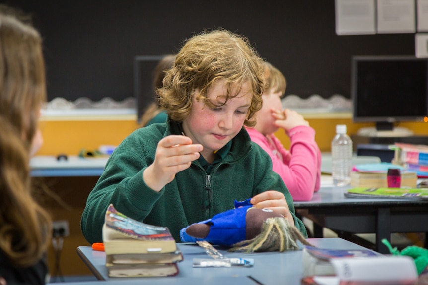 Student Max Kingston sews up a doll wearing blue clothing.