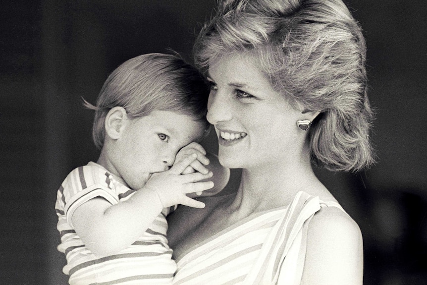 Princess Diana holds Prince Harry, who is sucking his thumb.