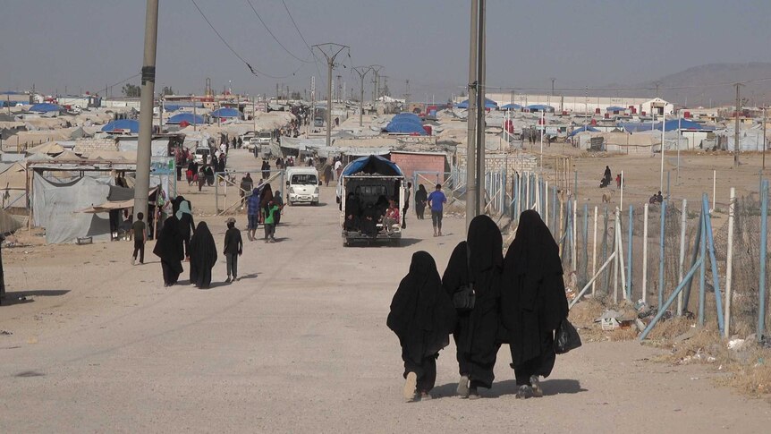 Two women and a girl walk in the distance dressed in black robes walking on a pebbly road.