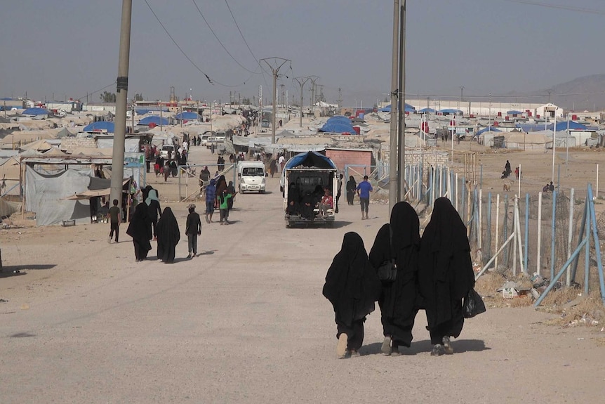 Two women and a girl walk in the distance dressed in black robes walking on a pebbly road.