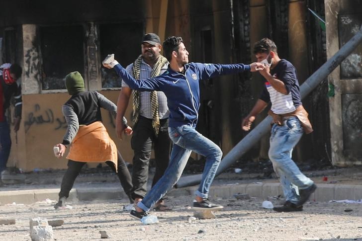 A man stands throwing a rock at US embassy protests in Baghdad.