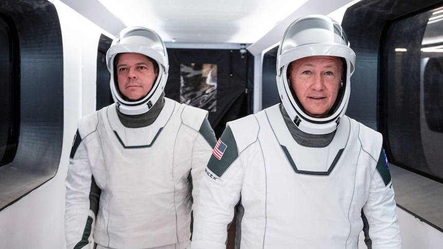 Two astronauts wearing space suits walk through a tunnel.