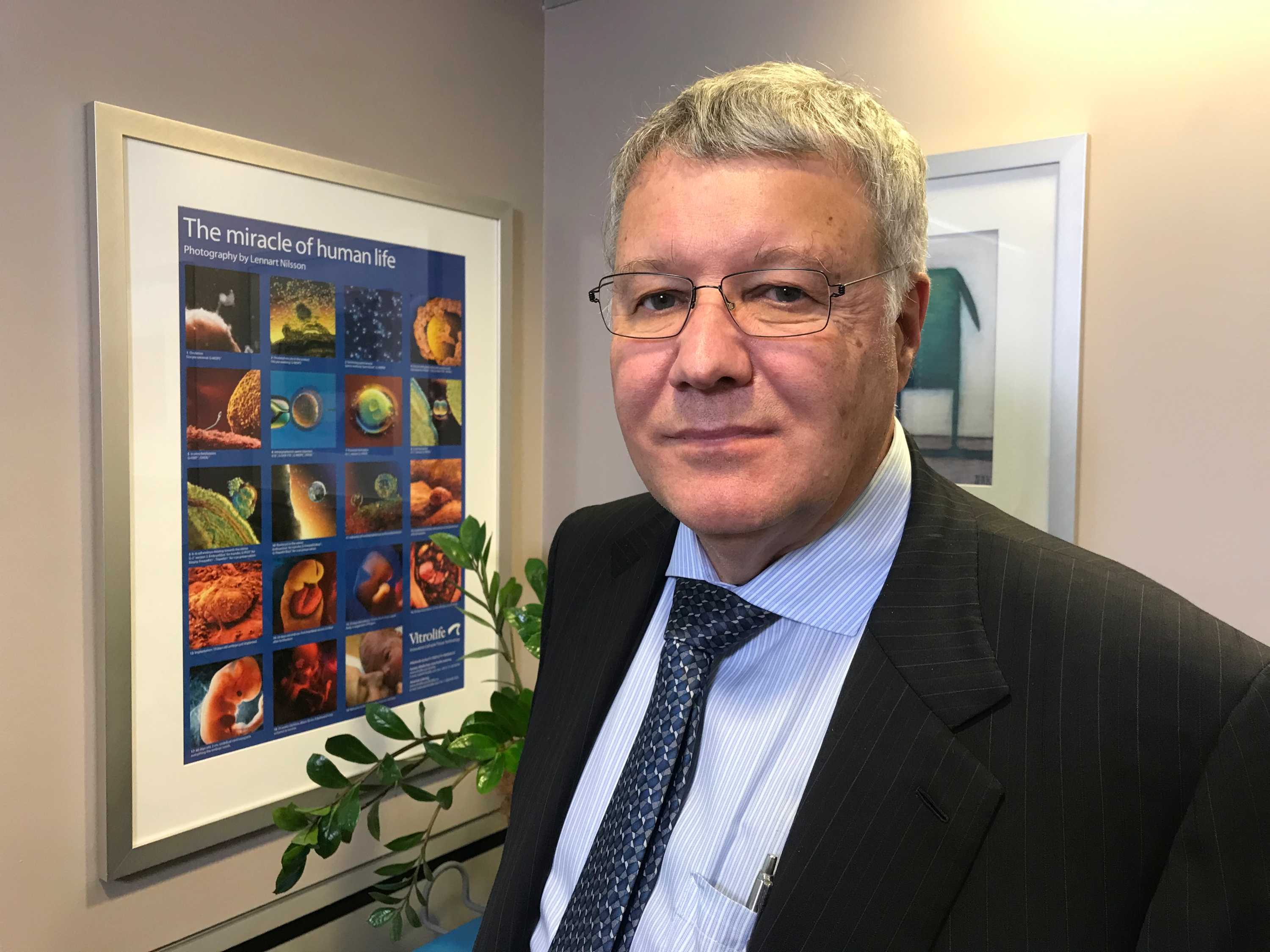 David Molloy in an office, next to a framed poster that says 'The Miracle of Human Life'