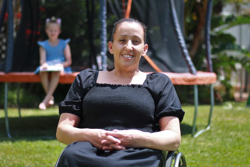 A woman sitting in a wheelchair infront of a trampoline in her backyard
