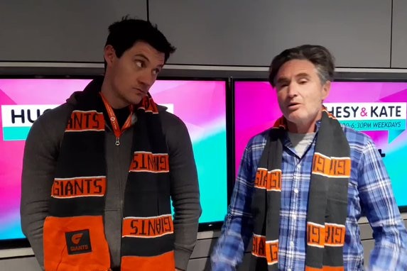 Ed Kavalee and Dave Hughes stand in a radio studio wearing GWS Giants scarves.